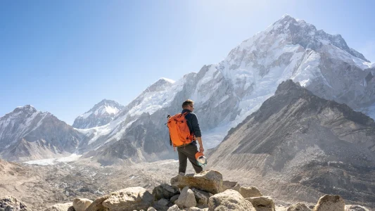 Narancssárga hátizsákos ember egy havas hegycsúcs előtt.