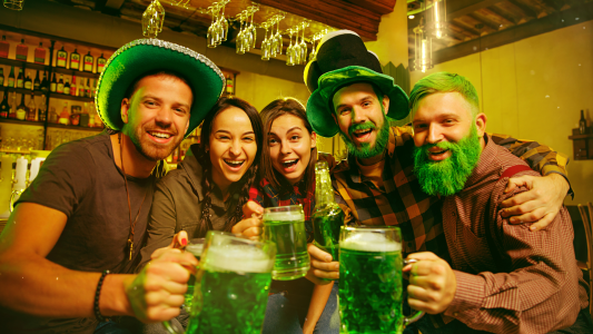 Zöld szinű sörrel koccintó emberek zöld kalapban.