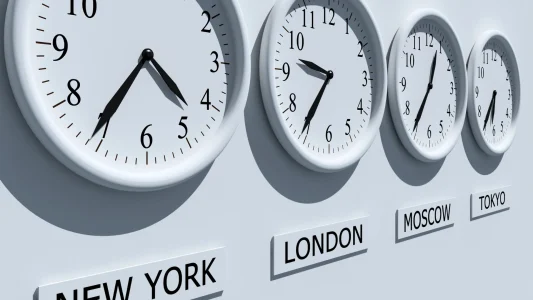 Több egyforma fehér falióra a falon, amik alatt más-más városnevek vannak, és az órák az adott város helyi idejét mutatják.